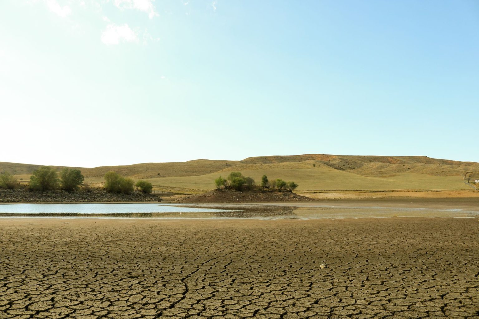 Corumbá registra 43,2°C e alerta para risco elevado de incêndios no Pantanal Paisagem árida com solo rachado, pouca vegetação e uma área de água sob céu claro.