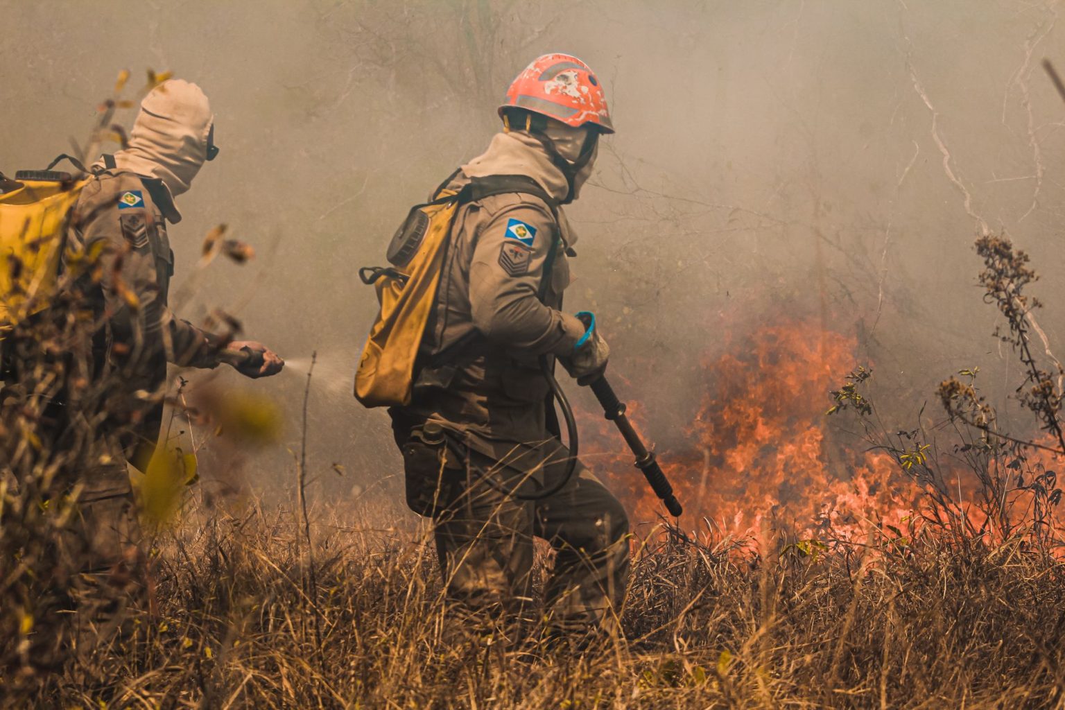 Bombeiros combatem um incêndio florestal em uma área de vegetação seca.